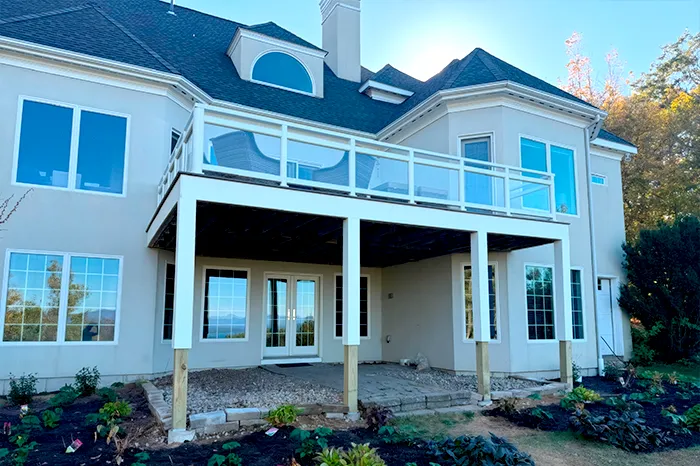 Two-story deck addition with a glass panel railing built over a covered patio